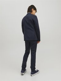 Completo blu con giacca su misura e pantaloni coordinati, arricchito da dettagli in cucitura bianca e sneakers blu casual.