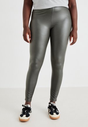 Green, high-shine leggings made of a stretchy material. Fitted design with a smooth texture, paired with black and white athletic shoes.