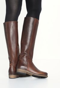 Bottes hautes en cuir marron avec une finition texturée, une fermeture éclair latérale et un petit talon en bois. Détails de couture accentués.