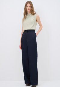 Ljusgrön ärmlös topp med rund halsringning, kombinerad med högmidjade, vida marinblå byxor; slät tyg, minimalistisk design.
