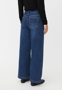 Vaqueros de pierna ancha en azul oscuro, con cintura alta, dos bolsillos traseros y un acabado limpio en el dobladillo. La textura de la tela parece resistente.