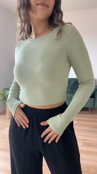 Top cropped canelado verde-claro com mangas longas, combinado com calças largas pretas. O top tem um design justo e um decote redondo.