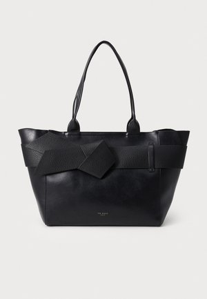Sort læder tote taske med lange håndtag og en bred tekstureret rem bundet i en sløjfe foran, mærket Ted Baker.