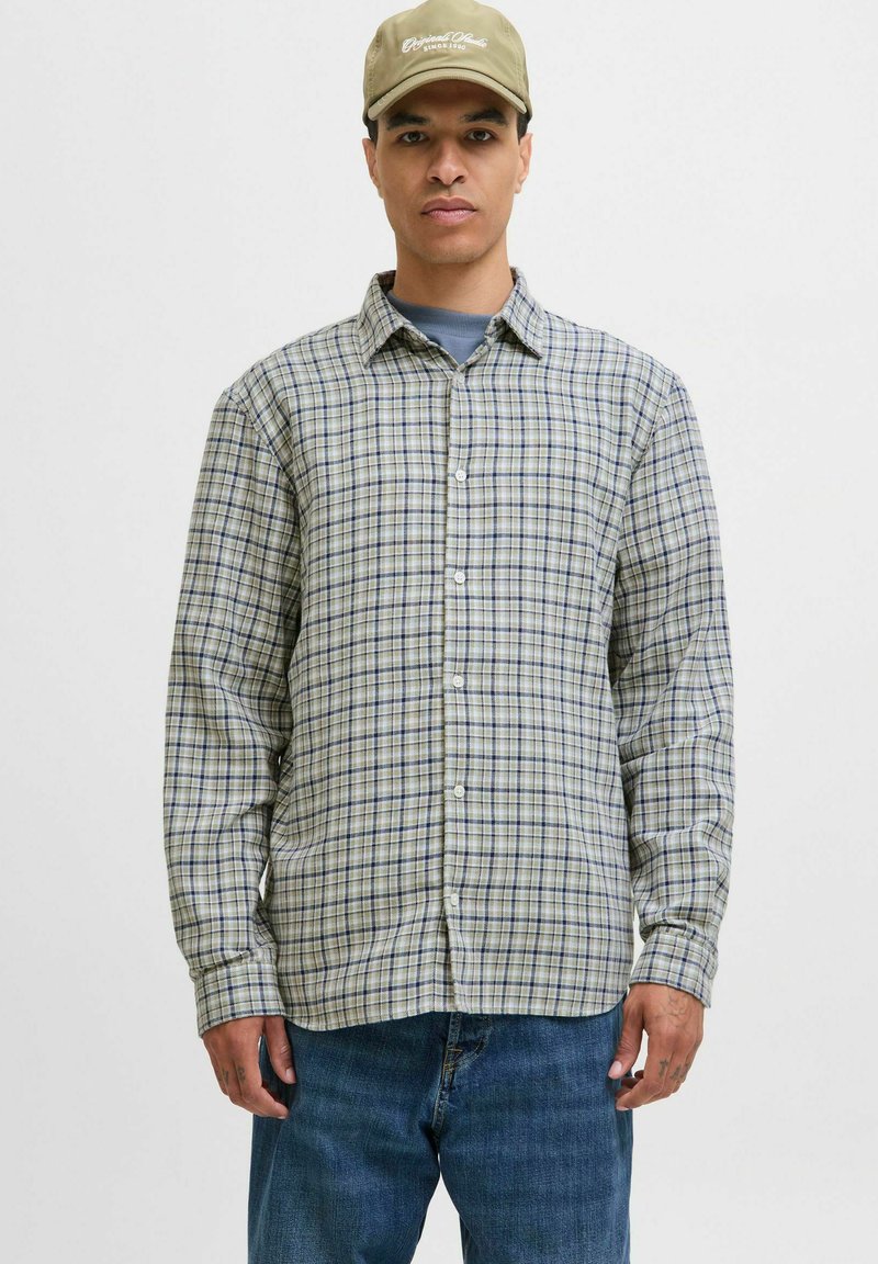 Chemise à manches longues avec un motif tartan vert et bleu, fabriquée en tissu léger. Associée à un jean en denim et une casquette.