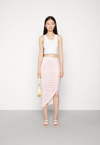 Top crop branco combinado com uma saia midi com mármore rosa, apresentando pregas e uma fenda lateral; modelo segura uma pequena mala amarela e usa sandálias brancas com tiras.