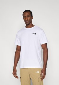 Λευκό βαμβακερό μπλουζάκι με κοντά μανίκια, στρογγυλή λαιμόκοψη και μαύρο λογότυπο στο αριστερό στήθος, συνδυασμένο με μπεζ παντελόνι cargo με φερμουάρ.