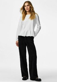 Hvit langermet peplum-topp med rund hals, kombinert med svarte vid bukser i kordfløyel og svarte platåsko.