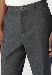 Pantaloni in misto lana di colore grigio scuro con motivo a trama, chiusura con bottone, pieghe frontali e tasche laterali, che mettono in risalto un design sartoriale.
