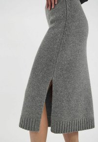 Jupe midi en tricot gris avec ourlet côtelé, fentes latérales et texture douce, présentant une coupe ajustée et un motif subtil sur l'ensemble.