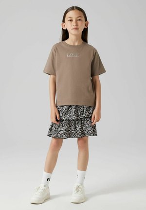 T-shirt di cotone marrone con "LOVE" stampato in colori chiari, abbinato a una gonna a balze tiered con stampa leopardata bianca e nera e sneakers bianche.