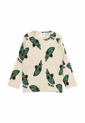 Haut à manches longues en crème avec un motif de feuilles vertes répétées, des lunettes de soleil noires et des accents de texte en noir.