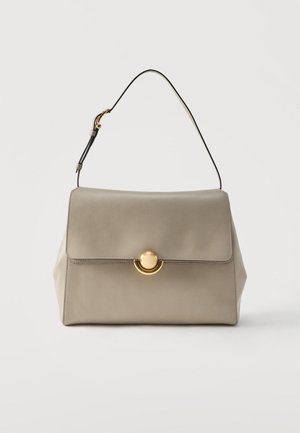 Sac à main en cuir beige avec une seule bandoulière noire et une fermeture circulaire dorée, présenté sur un fond blanc uni.