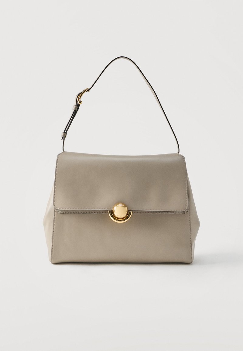 Μπεζ δερμάτινη τσάντα χειρός με μία μαύρη λουρίδα και χρυσό στρογγυλό κούμπωμα, παρουσιασμένη σε απλό λευκό φόντο.