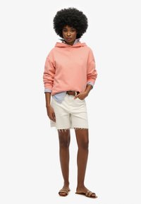 Sudadera rosa claro, camiseta de rayas azules debajo, pantalones cortos blancos con dobladillo deshilachado, cinturón marrón y sandalias marrones con acentos circulares.