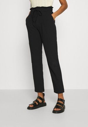 Sorte, højttaljede bukser med en flæset elastisk talje, sidelommer og tilspidsede ben, kombineret med sorte sandaler med stropper.