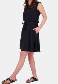 Abito nero senza maniche con bottoni, cintura regolabile in vita, tasche laterali e dettaglio di ricamo a forma di cuore, realizzato in tessuto leggero.