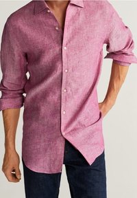 Roze linnen overhemd met lange mouwen, opgerolde manchetten, gestructureerde kraag en knoopsluiting aan de voorkant. Draagt over donkere denim broeken, die een gestructureerde afwerking tonen.