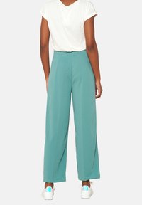Pantalones de pierna ancha turquesa con cintura alta y textura suave, combinados con una camiseta blanca y zapatillas blancas con acentos iridiscentes.