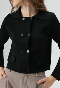 Zwarte cardigan met knopen en een kraag, uitgevoerd met zes knopen en twee voorzakken. Geribbelde textuur en een aansluitend model.