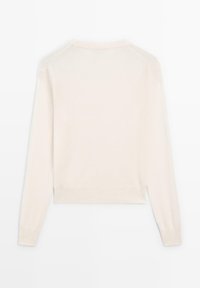 Krämfärgad tröja med långa ärmar, ribbade muddar och fåll, gjord av mjukt material som visar en enkel och slät textur.