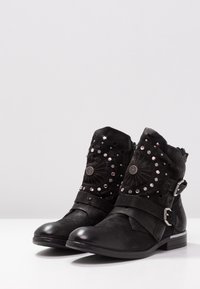 Black ankle boots made of leather with decorative studs and circular patterns, featuring two buckled straps and a low heel.