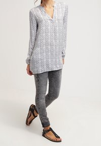 Blouse légère à motifs avec un col en V, associée à un jean skinny gris et des sandales noires à brides avec semelles plates.