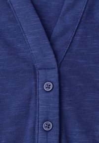 Primo piano della parte anteriore di un cardigan in maglia blu con due bottoni abbinati e tessuto strutturato intorno a un colletto a V.