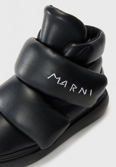 Čierna kožená členková obuv s vystuženým dizajnom, s bielym logom "Marni" a zakrivenými akcentmi pre zvýraznenie textúry. Okrúhla špička, plochá podrážka.