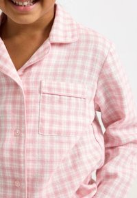 Lyserød flannel pyjamasoverdel med ternet mønster, der har en lomme og rund krave, afsluttet med hvid piping langs kanterne.