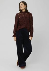 Blouse en dentelle bourgogne avec un col haut, des poignets à volants et une fermeture à boutons, associée à un pantalon large en velours côtelé bleu marine et des baskets marron.