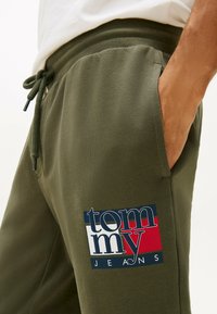 Olijfgroene joggers met een geribbelde tailleband en koord, met een rechthoekig logopatch in navy, rood en wit op de linker bovenbeen.