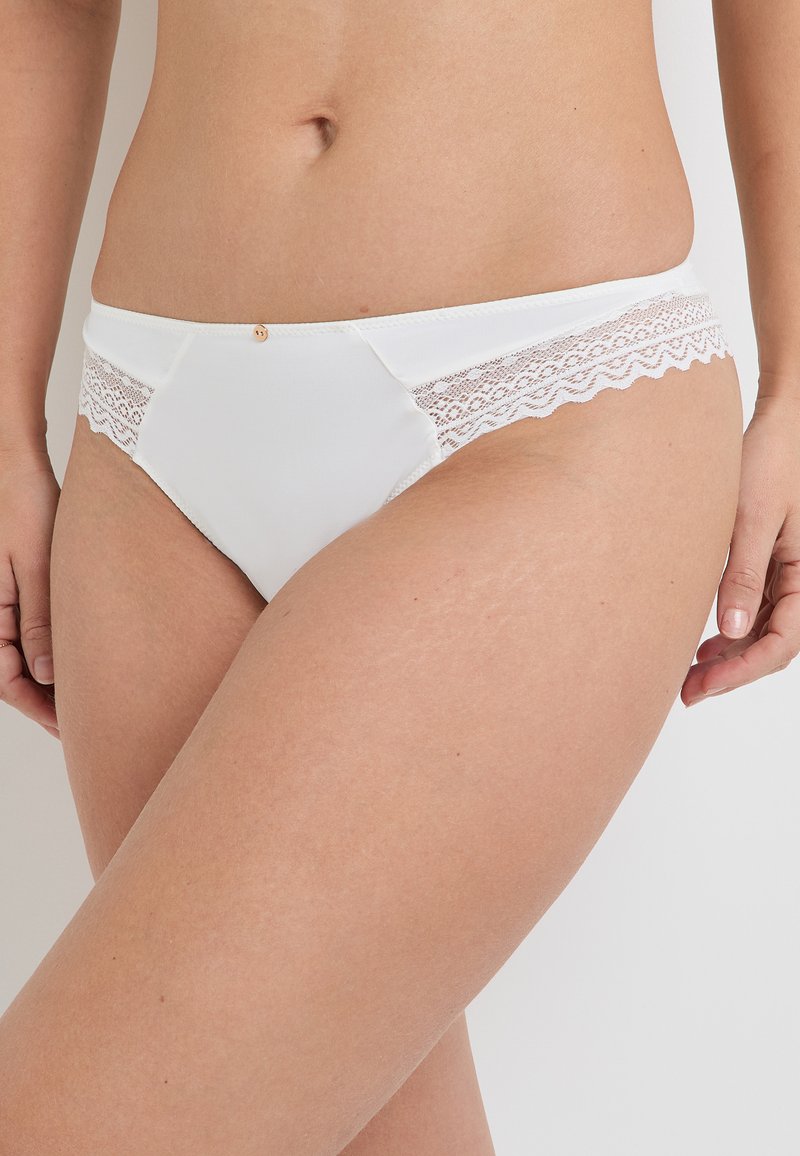 Culotte blanche en tissu doux, avec une délicate dentelle sur les côtés et un petit accent doré à l'avant.