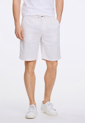 Shorts de lino blancos con corte relajado, cierre con cordón y bolsillos laterales, combinados con zapatillas blancas. Textura suave y ligera.