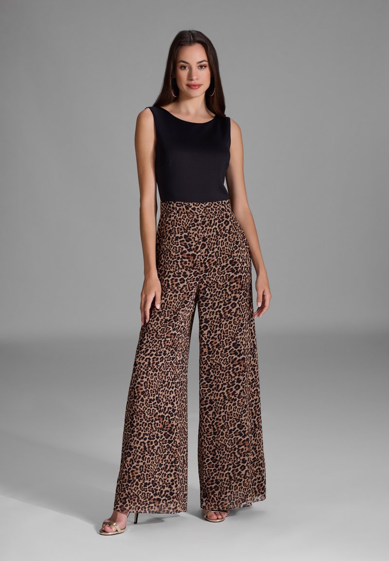Top noir sans manches associé à un pantalon large à imprimé léopard. Tissu texturé avec un motif naturel. Modèle portant des sandales ouvertes.