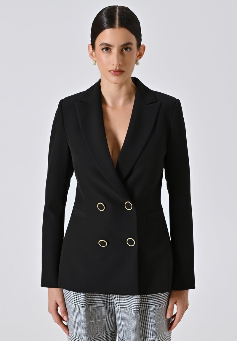 Zwarte dubbelzijdige blazer met gouden ovale knopen, scherpe revers en een op maat gemaakte pasvorm, gecombineerd met geruite broeken. Gladde stofafwerking.