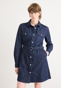 Denim shirt dress in dark blue with long sleeves, button front, two chest pockets, and belted waist. Features a clean, classic design.