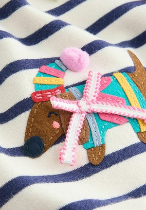 Gestickter Aufnäher eines braunen Hundes auf einem cremefarbenen und marineblauen gestreiften Stoff, mit bunten Filzdekorationen und einem rosa Pompon-Akzent.