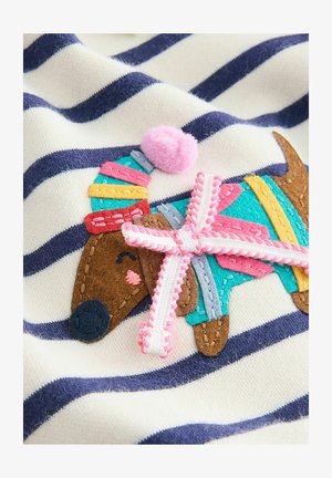 Gestickter Aufnäher eines braunen Hundes auf einem cremefarbenen und marineblauen gestreiften Stoff, mit bunten Filzdekorationen und einem rosa Pompon-Akzent.