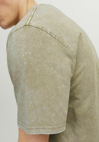 Lys oliven grøn kortærmet t-shirt med en falmet tekstur, rund halsudskæring og synlige sømdetaljer på skulderen og kanten.