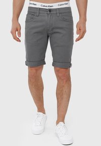 Grå denim shorts med opfoldede manchetter, der har en knaplukning og forlommer. Taljen viser et hvidt Calvin Klein-logo.