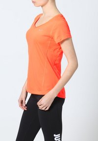 Lysorange kortärmad träningströja med V-ringning och texturerade sidopaneler, i kombination med åtsittande svarta leggings med vit text.