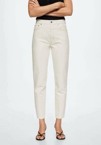 Jeans en denim couleur crème, à taille fuselée. Comprend des poches avant, une fermeture éclair et une texture lisse. Associés à des sandales noires.