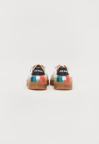 Weiße Leinenschuhe mit einem mehrfarbigen karierten Muster an der Ferse, brauner Gummisohle und schwarzem Markenetikett auf der Rückseite.