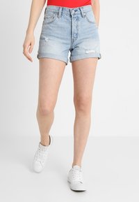 Vaaleansiniset farkkushortsit, joissa on kulutettu muotoilu ja käänteet, korkealla vyötäröllä ja viidellä taskulla. Yhdistetty valkoisiin tennareihin.