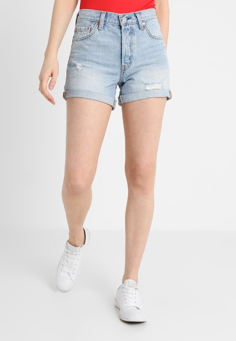 Vaaleansiniset farkkushortsit, joissa on kulutettu muotoilu ja käänteet, korkealla vyötäröllä ja viidellä taskulla. Yhdistetty valkoisiin tennareihin.