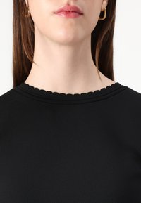 Top nero con texture a coste e scollatura a onde, con maniche corte e design aderente, indossato in vista ravvicinata.