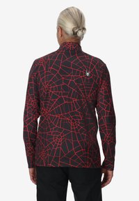 Zwarte langemouwen shirt met een rood spinnenwebpatroon. Voorzien van een hoge kraag en een klein spinlogo op de bovenrug. Rekbare en gladde textuur.