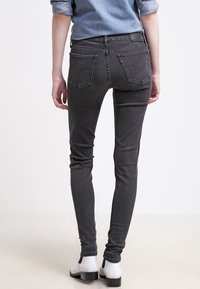 Slim-fit grå denimjeans med mjuk textur, hög midja, två bakfickor och subtila sömdetaljer, i kombination med vita ankelskor.