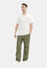 Polo bianco con colletto e maniche corte, abbinato a pantaloni cargo verde oliva larghi e sneakers bianche.