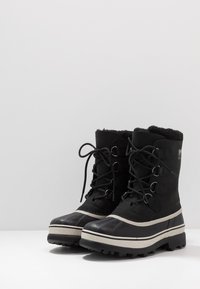 Schwarze Winterstiefel mit abgerundetem Zehenbereich, Schnürung an der Vorderseite, Fellfutter am Knöchel und Gummi-Außensohle mit tiefen Profil für besseren Halt.